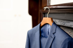 Blue suit jacket hanging on a wooden hanger against a blurred background
