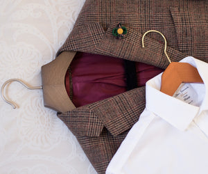 Brown plaid jacket on a hanger with a white shirt underneath on a textured surface