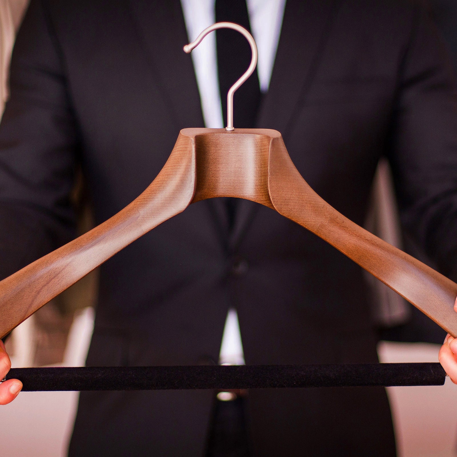 Wooden hanger held by a person in a tuxedo with a blurred background